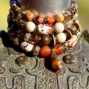 May include: A stack of colorful beaded bracelets with brown, orange, white, and gold beads. The bracelets are layered on top of each other and have a variety of textures and patterns.