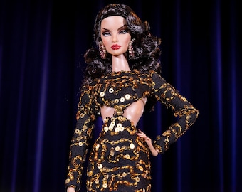 May include: A fashion doll wearing a black and gold sequined dress with a cut-out design. The doll has long black hair and is wearing black heels.