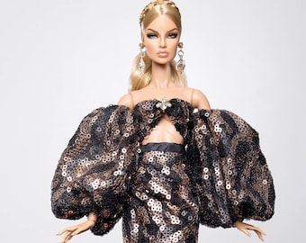 May include: A doll wearing a black and gold sequined gown with a high slit and large, puffed sleeves. The gown has a fitted bodice and a flowing skirt.