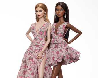 Puede incluir: Dos muñecas de moda con vestidos de estampado floral. La muñeca de la izquierda lleva un vestido largo y fluido con una abertura alta. La muñeca de la derecha lleva un vestido más corto con un dobladillo con volantes. Ambas muñecas llevan tacones altos rosas.