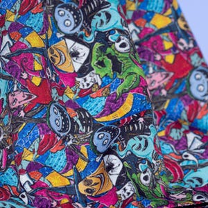 May include: Close-up of a fabric with a colorful, cartoonish design. The pattern features various characters in shades of blue, green, yellow, red, and purple. The fabric appears to be folded, revealing the intricate details of the print.