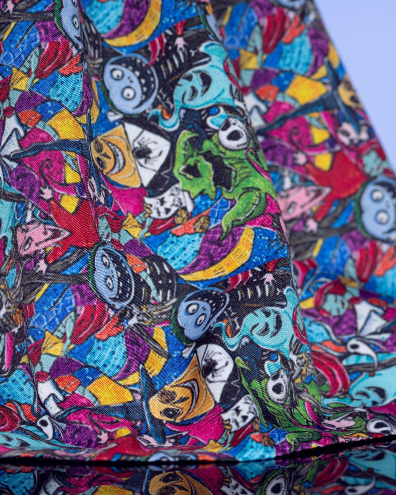 May include: Close-up of a fabric with a colorful, cartoonish design. The pattern features various characters in shades of blue, green, yellow, red, and purple. The fabric appears to be folded, revealing the intricate details of the print.