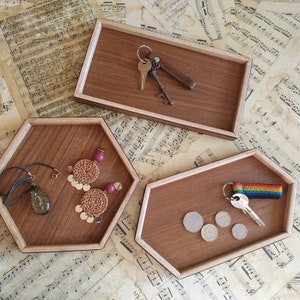 Può includere: Tre vassoi in legno con bordi arrotondati. I vassoi sono in legno scuro con un bordo in legno chiaro. Il vassoio superiore ha un portachiavi con una chiave e un'etichetta che dice "Three Years With You". Il vassoio centrale ha una collana con un ciondolo e due orecchini. Il vassoio inferiore ha una chiave e un nastro arcobaleno.