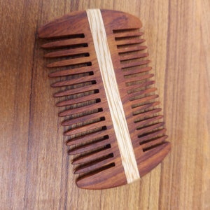 Könnte beinhalten: Ein Holzkamm mit einem hellbraunen Streifen in der Mitte. Der Kamm hat eine abgerundete Form und ist aus dunkelbraunem Holz gefertigt.