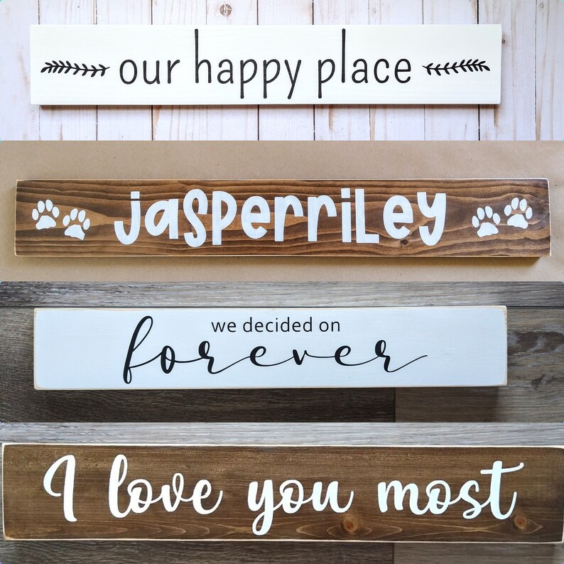 May include: Four rectangular wooden signs with text. The top sign is white with black text reading 'our happy place'. The second is dark brown with white text 'JASPERRILEY' and paw prints. The third is white with black text 'we decided on forever'. The bottom is dark brown with white text 'I love you most'.