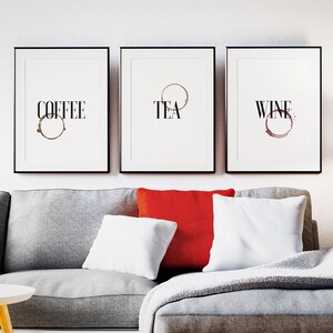 May include: Three black framed prints with white backgrounds and black text. The prints read "Coffee", "Tea", and "Wine" with a brown, gold, and red ring stain, respectively, underneath each word.
