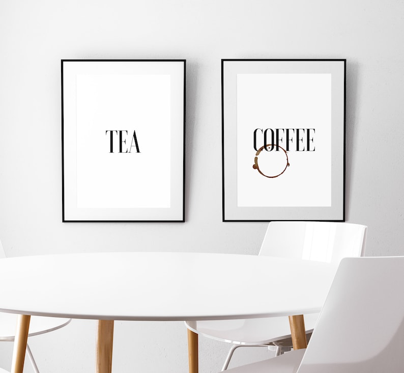 May include: Two black framed prints on a white wall. The print on the left says "TEA" in black text. The print on the right says "COFFEE" in black text with a brown coffee ring underneath.