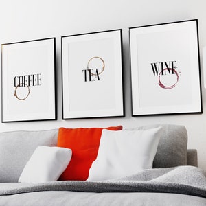 May include: Three framed prints with black frames and white mats. The prints feature the words "COFFEE", "TEA", and "WINE" with a coffee stain, tea stain, and wine stain, respectively.