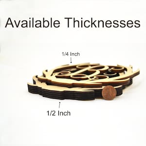 Puede incluir: Primer plano de un monograma de madera con cuernos de ciervo, que muestra los diferentes espesores disponibles. El monograma tiene un grosor de 1/4 de pulgada y 1/2 pulgada. Se incluye una moneda de un centavo para la escala.
