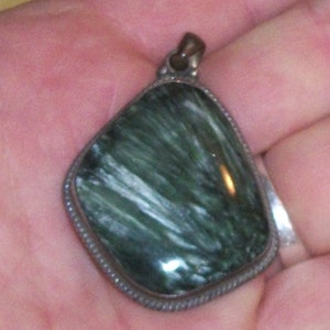 Puede incluir: Un colgante de plata con una piedra verde y blanca. La piedra tiene un patrón estriado.