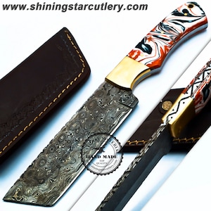 May include: A Damascus steel knife with a patterned blade and a handle featuring orange, white, and black swirls. The knife has a gold-colored bolster and comes with a brown leather sheath. The text "HAND MADE TOP QUALITY" is visible.