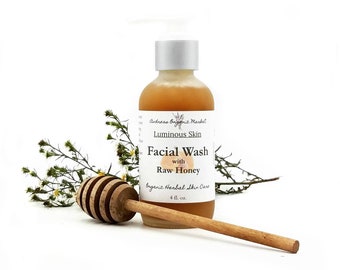 May include: A 4-ounce bottle of facial wash with raw honey. The bottle is amber colored and has a white label with the text "Andreas Organic Market", "Luminous Skin", "Facial Wash with Raw Honey", and "Organic Herbal Skin Care". A wooden honey dipper is in the foreground.