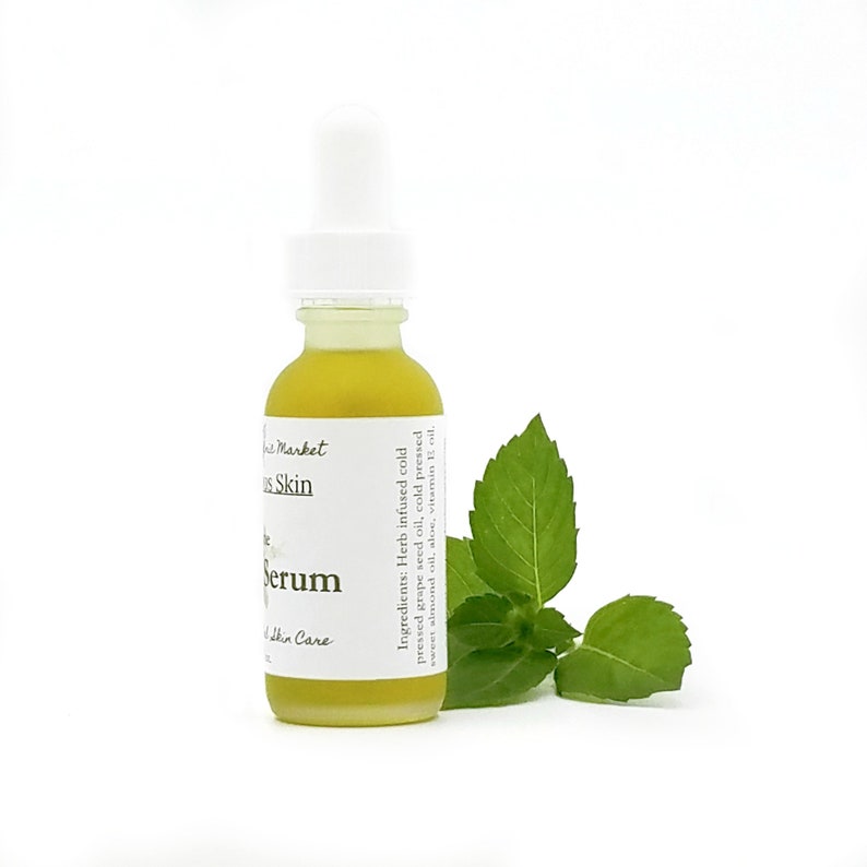 Puede incluir: Una botella de vidrio transparente con un gotero blanco en la parte superior, llena de un l&iacute;quido amarillo. La botella est&aacute; etiquetada como "Skin Market Serum" y enumera los ingredientes: "Aceite de semilla de uva infundido en fr&iacute;o prensado en fr&iacute;o, aceite de almendras dulces prensado en fr&iacute;o, aloe vera, aceite de vitamina E". Una ramita de hojas de menta verde est&aacute; al lado de la botella.