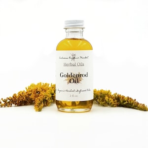 May include: A clear glass bottle filled with goldenrod oil, labeled "Goldenrod Oil" and "2 fl oz." The bottle is positioned in front of dried yellow flowers. The label also reads "Andreas Organic Market" and "Herbal Oils."