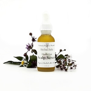 May include: A small amber glass bottle with a white dropper top and a white label. The label reads "Andreas Organic Market Herbal Baby Cradle Cap Scalp Serum Organic Herbal Skin Care 1 fl. oz."