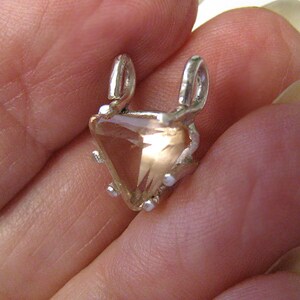 May include: A silver pendant with a triangular, peach-colored gemstone. The pendant has two loops at the top and small silver accents around the gem. The gemstone is faceted, catching the light and creating a sparkling effect.