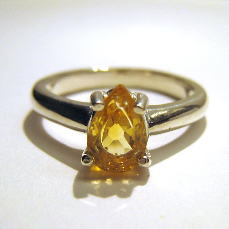 Puede incluir: Un anillo de plata con una piedra preciosa amarilla en forma de pera.