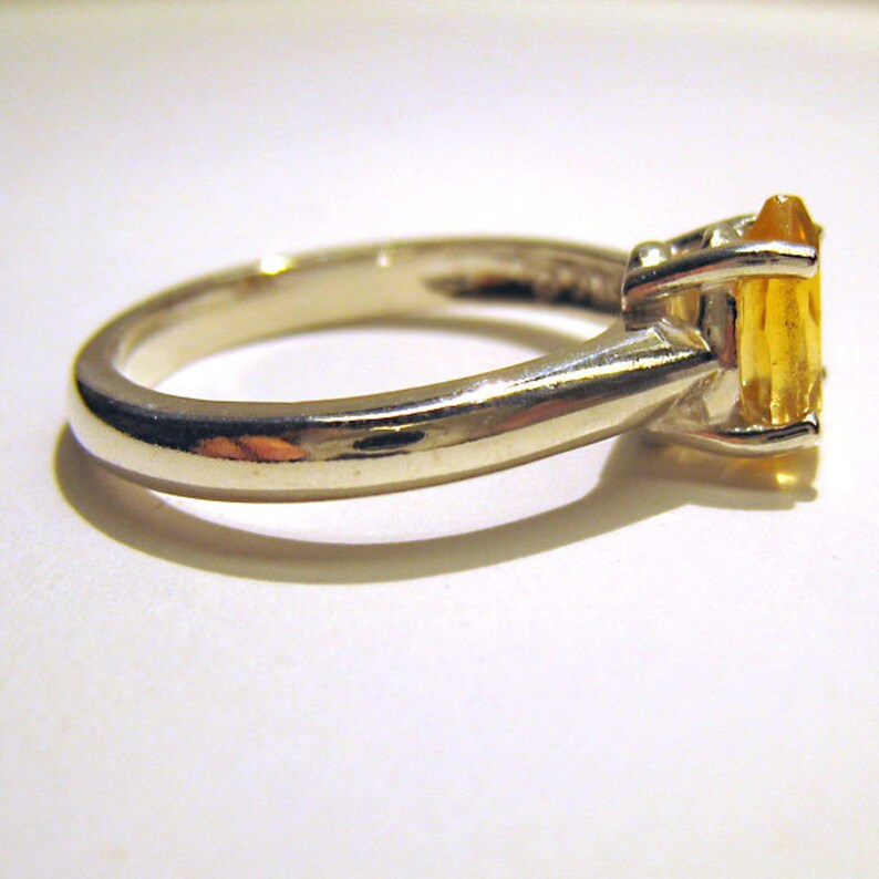 Puede incluir: Un anillo de plata con una piedra preciosa amarilla engastada en garras.