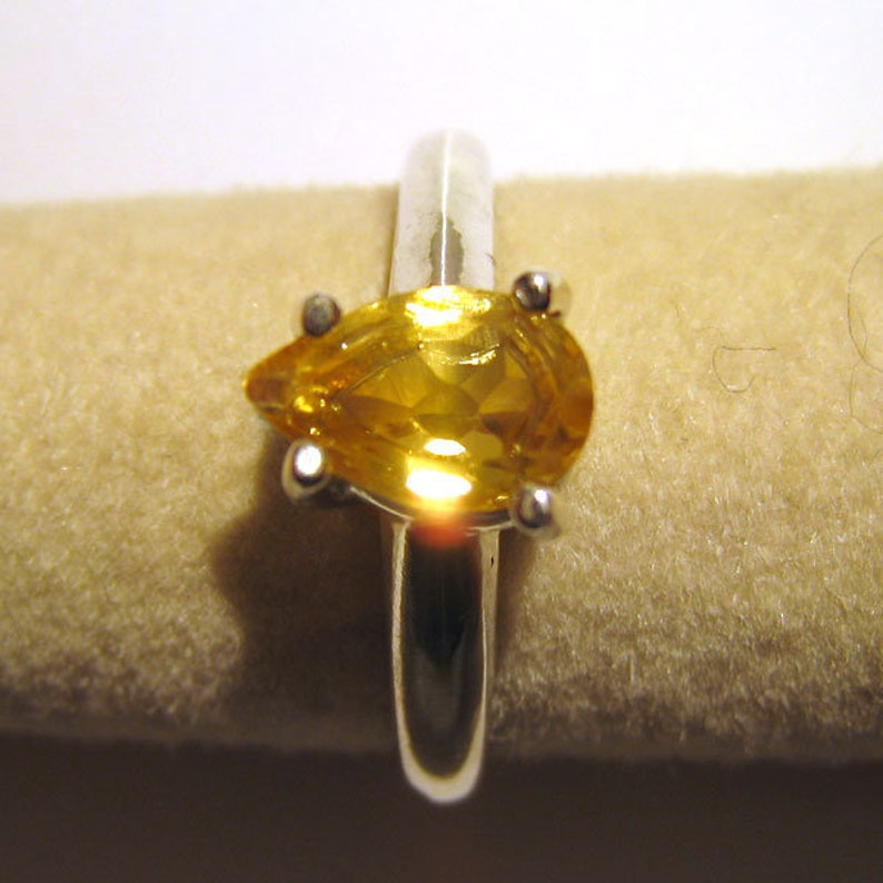 Puede incluir: Un anillo de plata con una piedra preciosa amarilla en forma de pera.