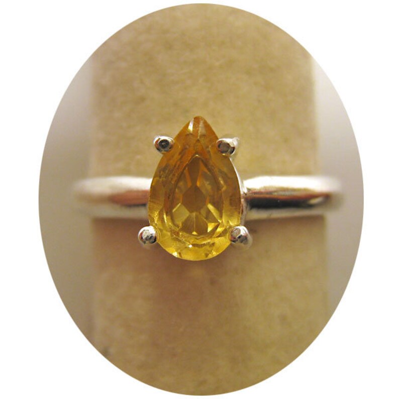 Puede incluir: Un anillo de plata con una piedra preciosa amarilla en forma de pera.