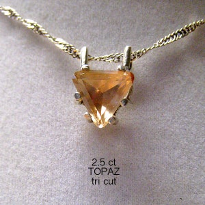 May include: A gold-toned necklace featuring a triangular, amber-colored topaz pendant. The pendant is held by a silver setting and suspended from a delicate chain. The text on the image reads "2.5 ct TOPAZ tri cut".