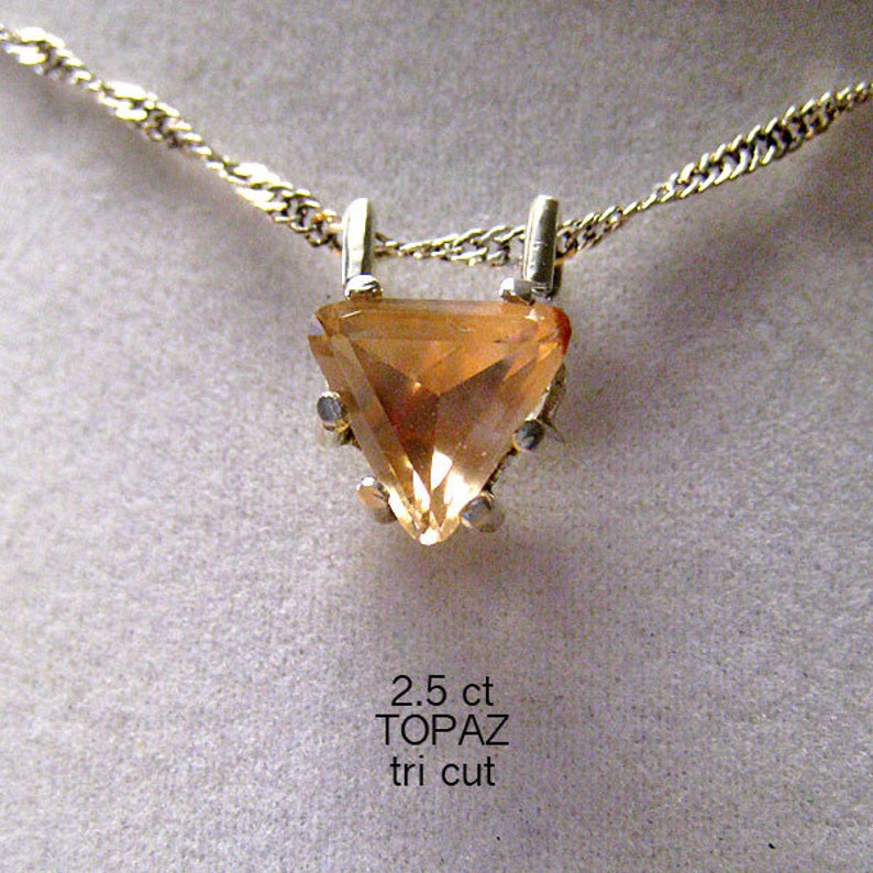 May include: A gold-toned necklace featuring a triangular, amber-colored topaz pendant. The pendant is held by a silver setting and suspended from a delicate chain. The text on the image reads "2.5 ct TOPAZ tri cut".