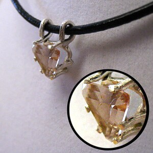 May include: A silver pendant with a heart-shaped, light brown gemstone. The pendant is suspended from a black cord necklace. A close-up shows the intricate details of the gemstone and the silver setting.