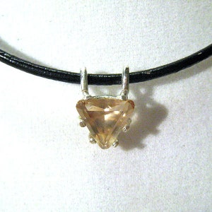 May include: A pendant necklace featuring a triangular, light brown gemstone set in a silver-colored metal. The pendant hangs from a black cord, creating a simple yet elegant design. The gemstone has multiple facets, reflecting light.
