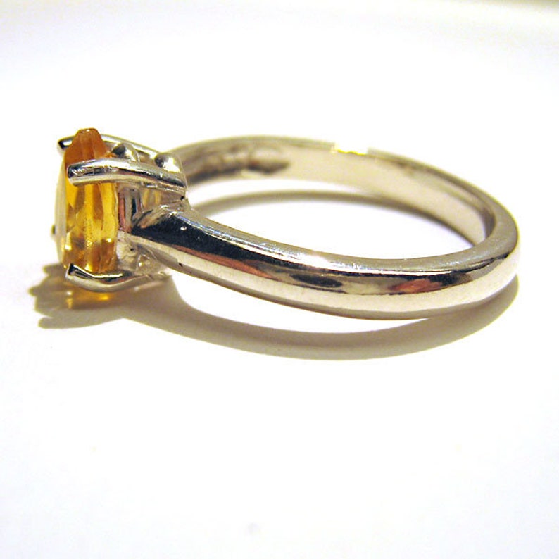 Puede incluir: Un anillo de plata con una piedra ovalada amarilla. El anillo tiene una banda simple y un acabado liso.