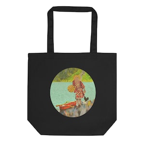 May include: A black tote bag with a circular design featuring a person in a red and gold costume standing on a rock by a lake. The person is holding a round object and there is a red boat in the water.