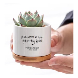 May include: White ceramic planter with a succulent plant. The planter has a bamboo base and a black inscription that reads "Heaven needed an Angel God picked my father Michael Stevenson 1958-2022".