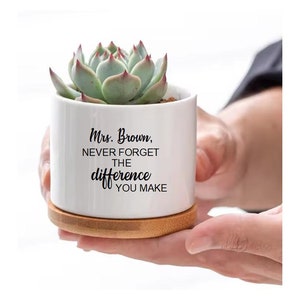 May include: White ceramic planter with a succulent plant and a bamboo base. The planter has the text "Mrs. Brown, Never Forget The Difference You Make" printed on it.