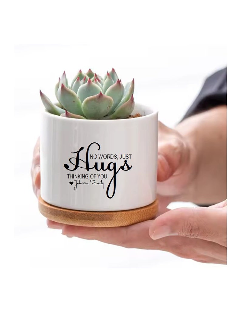May include: White ceramic succulent planter with a bamboo base. The planter has black text that reads 'Hugs, No words, just thinking of you, Johnson Family'.