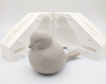 May include: A white two-piece mold for making a bird figurine. The mold is open and a gray bird figurine is sitting in front of it. The mold is labeled "HOTCAKESUSA.com" and "Candy".