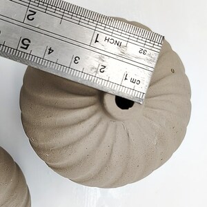 May include: Two small, brown, ceramic planters with a fluted design. The planters are approximately 2 inches in diameter. A ruler is used to show the size of the planters.