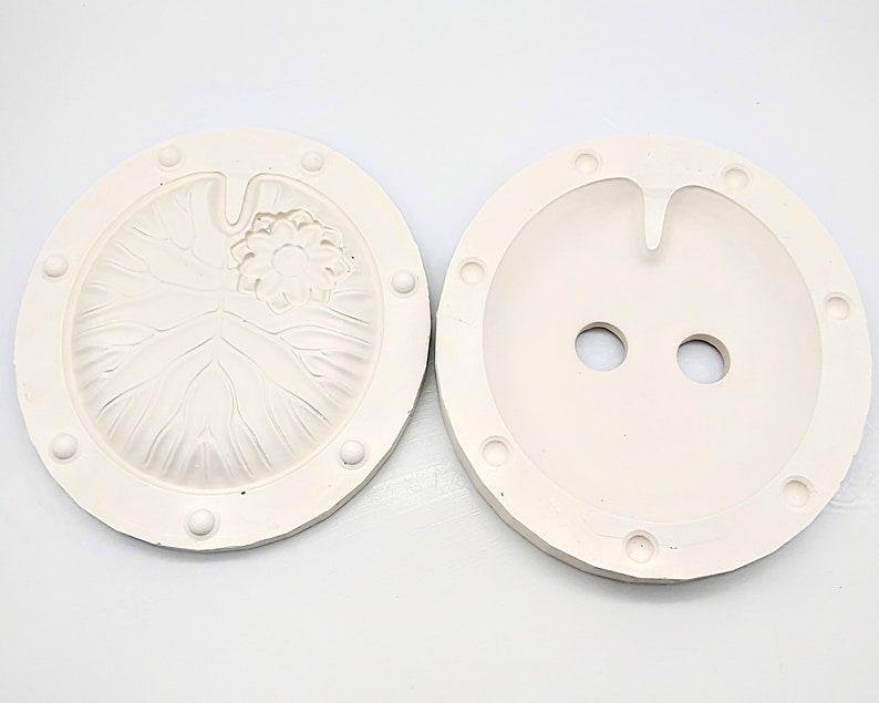 May include: Two white silicone molds for making resin crafts. One mold features a detailed lotus flower design, while the other has two round holes.