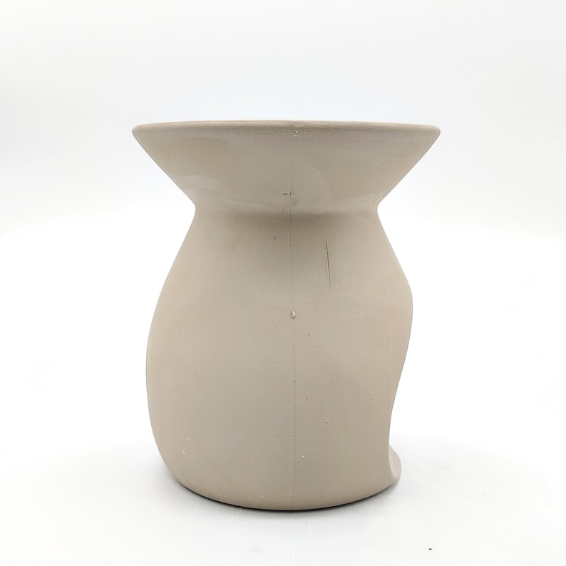 May include: A beige ceramic wax warmer with a wide, round opening at the top and a curved, open design on the side.