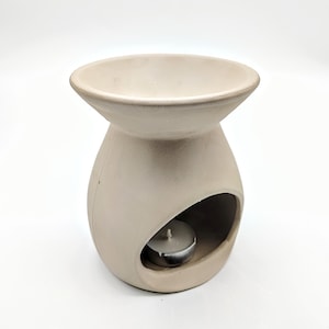May include: A white ceramic oil diffuser with a round top and a small opening for a tea light candle. The diffuser has a round base with a cutout for the candle.