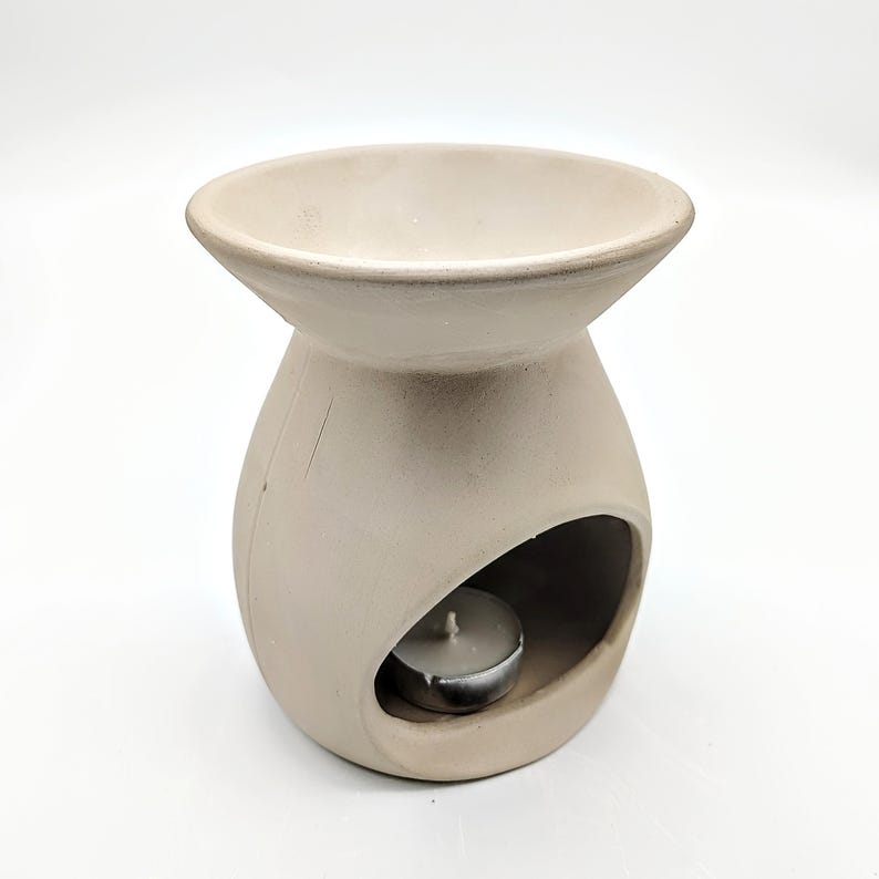 May include: A white ceramic oil diffuser with a round top and a small opening for a tea light candle. The diffuser has a round base with a cutout for the candle.