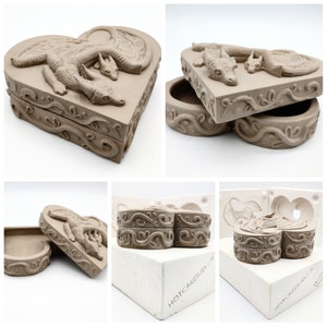 May include: A two-piece heart-shaped mold for making a dragon-themed jewelry box. The mold is made of white silicone and has a smooth surface. The mold is labeled "HOTCAKESUSA" on the bottom. The finished jewelry box is made of brown clay and features a dragon and a baby dragon.