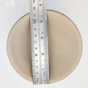 May include: A beige ceramic bowl with a diameter of 5 inches. The bowl is shown next to a ruler for size reference.
