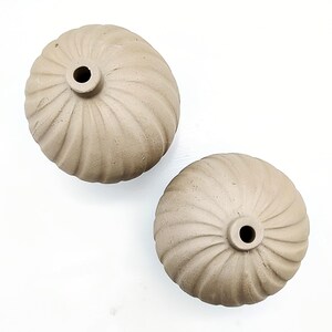 May include: Two beige ceramic vases with a ribbed design. The vases are round and have a small opening at the top.