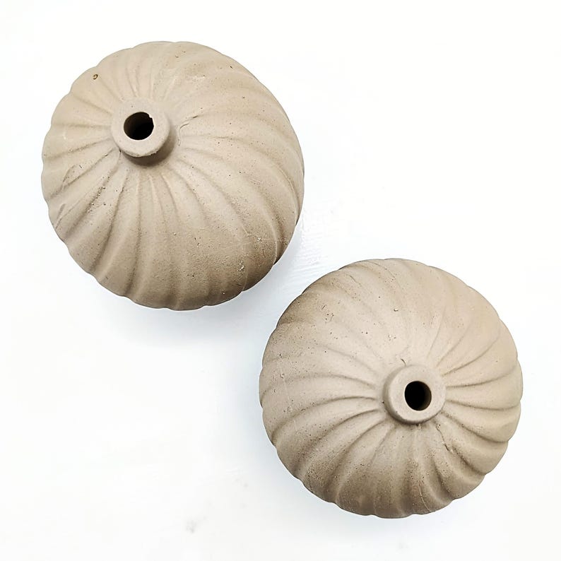 May include: Two beige ceramic vases with a ribbed design. The vases are round and have a small opening at the top.