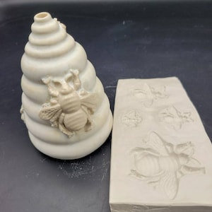 May include: A white ceramic beehive with a bee design, and a white silicone mold with bee designs.
