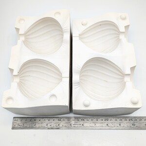 May include: Two-part white ceramic mold for making two pear-shaped objects. The mold is made of two halves that fit together to create a seamless shape.