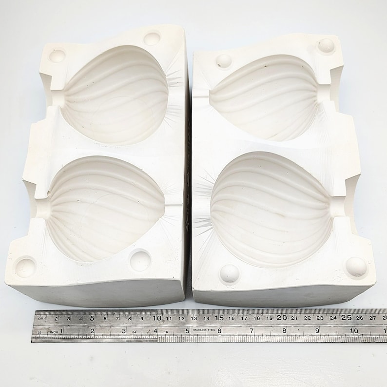 May include: Two-part white ceramic mold for making two pear-shaped objects. The mold is made of two halves that fit together to create a seamless shape.