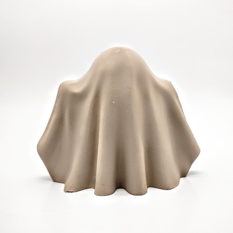 May include: A beige concrete ghost sculpture with a draped sheet design.