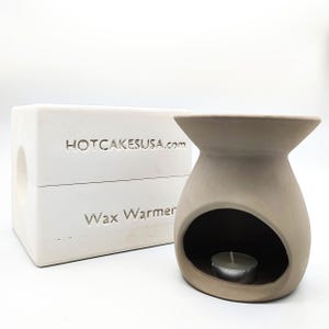 May include: White ceramic wax warmer with a round opening for a tea light candle. The warmer is labeled "Wax Warmer" and "HOTCAKESUSA.com".