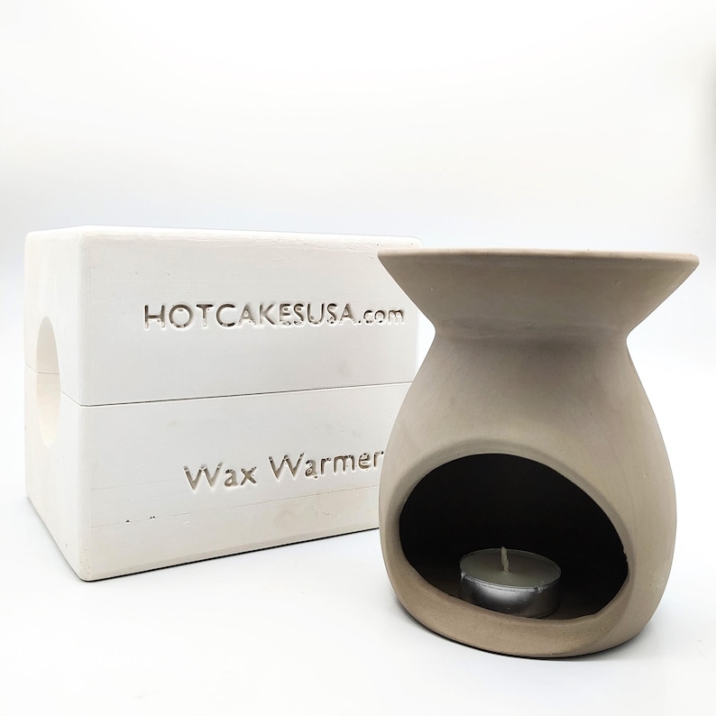 May include: White ceramic wax warmer with a round opening for a tea light candle. The warmer is labeled "Wax Warmer" and "HOTCAKESUSA.com".