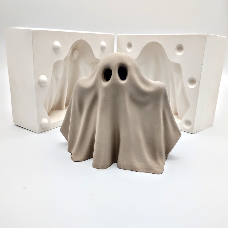 May include: A ceramic ghost mold for making Halloween decorations. The mold is white and has a smooth surface. The ghost is in a classic sheet-like shape with two black eyes.